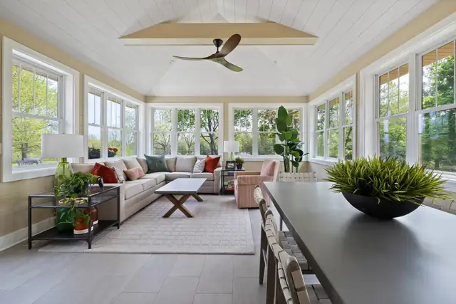 Three-season room addition with a white plank ceiling, a ceiling fan, a sectional sofa and windows on three sides