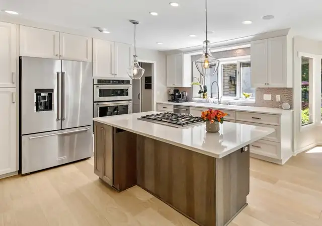 White kitchen with stained wood island, quartz counters, stainless refrigerator and double wall ovens