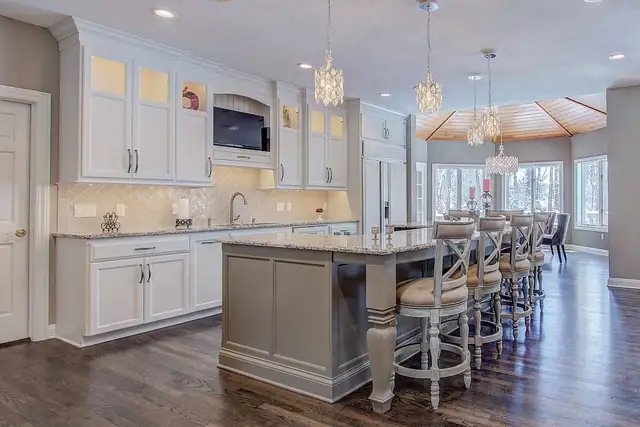 White kitchen with gray island and turned legs, crystal pendants and a sunroom dining area beyond