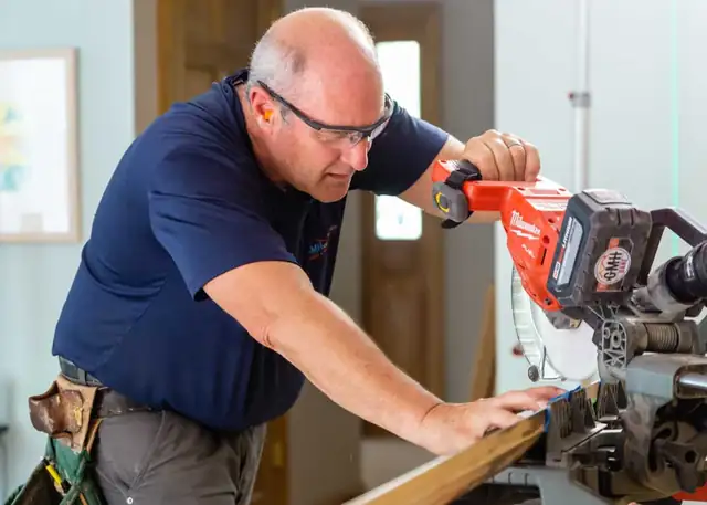 GMH Construction carpenter in safety glasses cutting trim with a miter saw