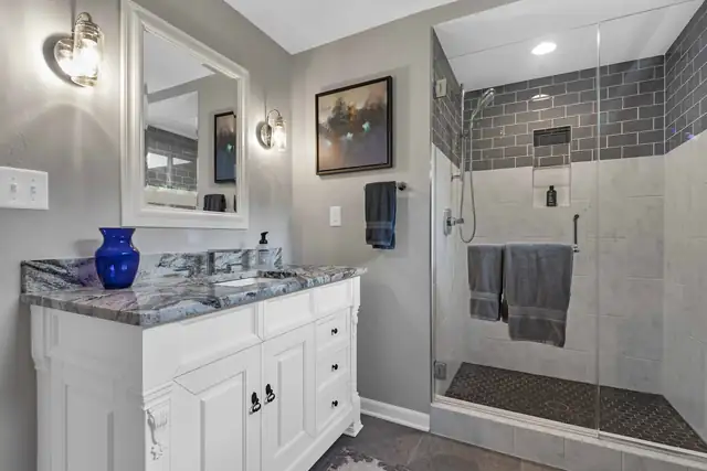 Three-quarter bathroom remodel with glass walk-in shower, gray subway tile accent, white vanity and granite top