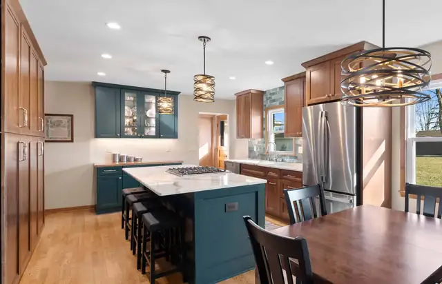 Kitchen with stained wood cabinets, a teal island and glass cabinets, a ring chandelier and a stainless refrigerator
