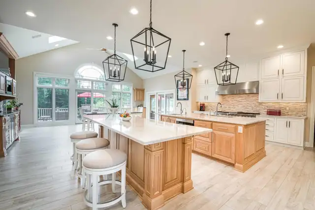 Bright kitchen with two light wood islands, white cabinets, lantern pendants and a vaulted ceiling