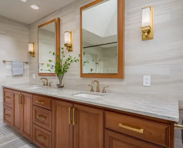 Primary bathroom remodel with cherry double vanity, marble-look top, brass mirrors and sconces