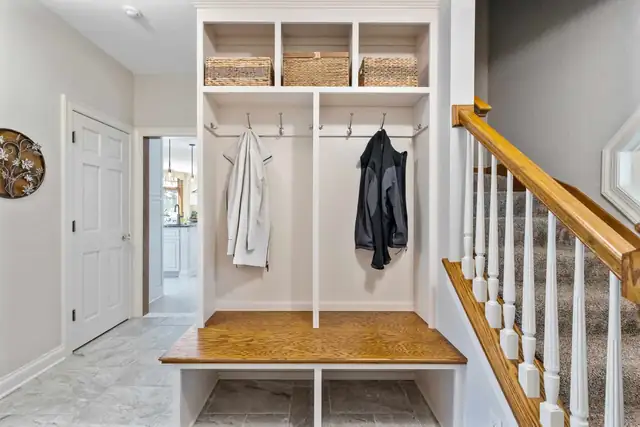 Mudroom with built-in bench, coat hooks and woven baskets in open cubbies beside the stairs
